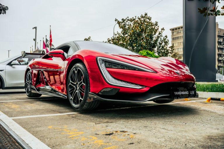 Dynamic shot of a vibrant red YangWang U9 sports car parked in an urban environment.