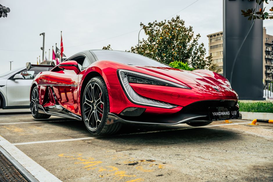 Dynamic shot of a vibrant red YangWang U9 sports car parked in an urban environment.