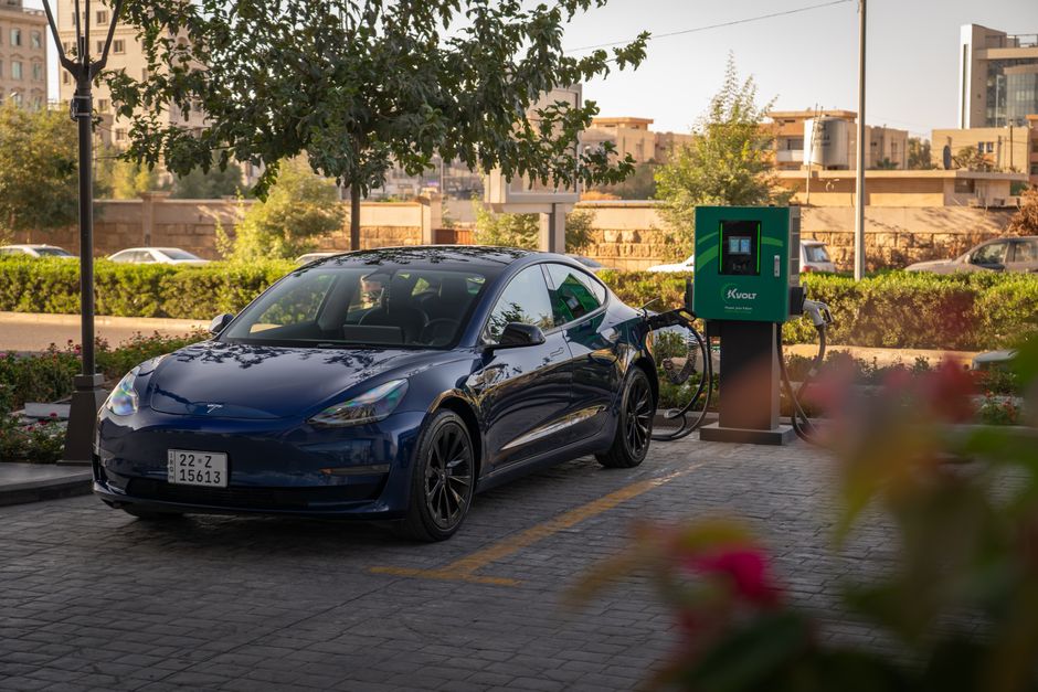 Tesla Model 3 charging at an urban electric vehicle station during daytime.