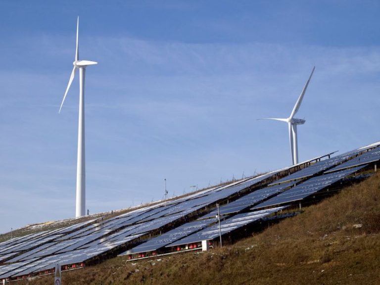 Wind turbines and solar panels on a hillside harnessing renewable energy under a clear sky.