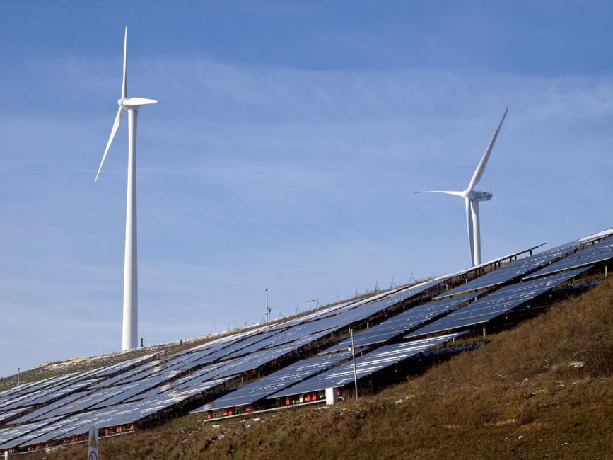 Wind turbines and solar panels on a hillside harnessing renewable energy under a clear sky.