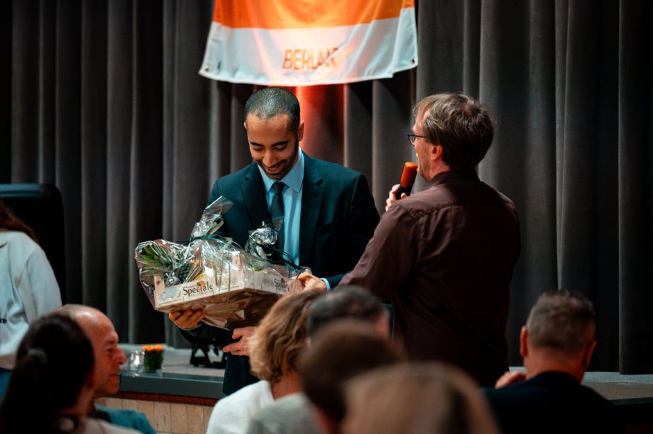 A man receives a gift basket during an award ceremony indoors, creating a celebratory atmosphere.