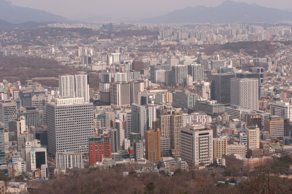 Aerial view of the bustling Seoul cityscape with modern skyscrapers and distant mountains.
