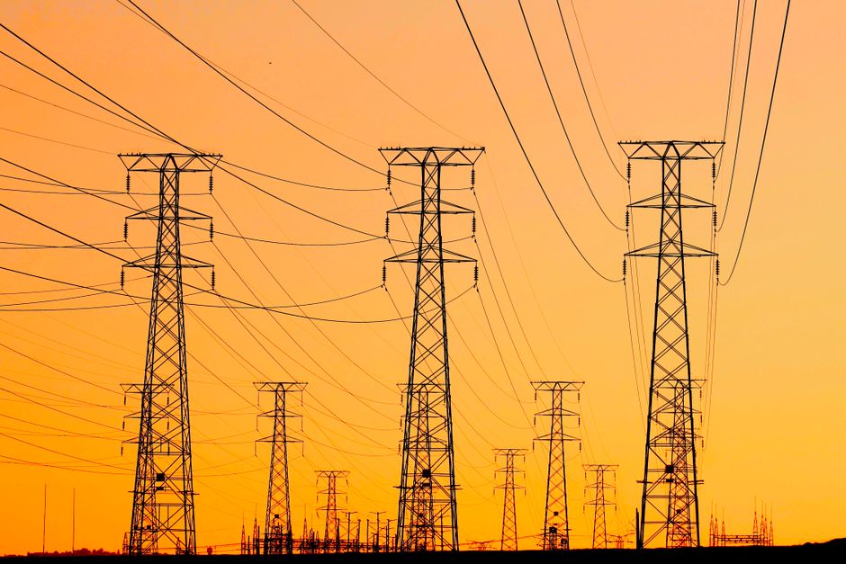 Silhouetted power lines against a vibrant orange sunset, symbolizing energy and infrastructure.