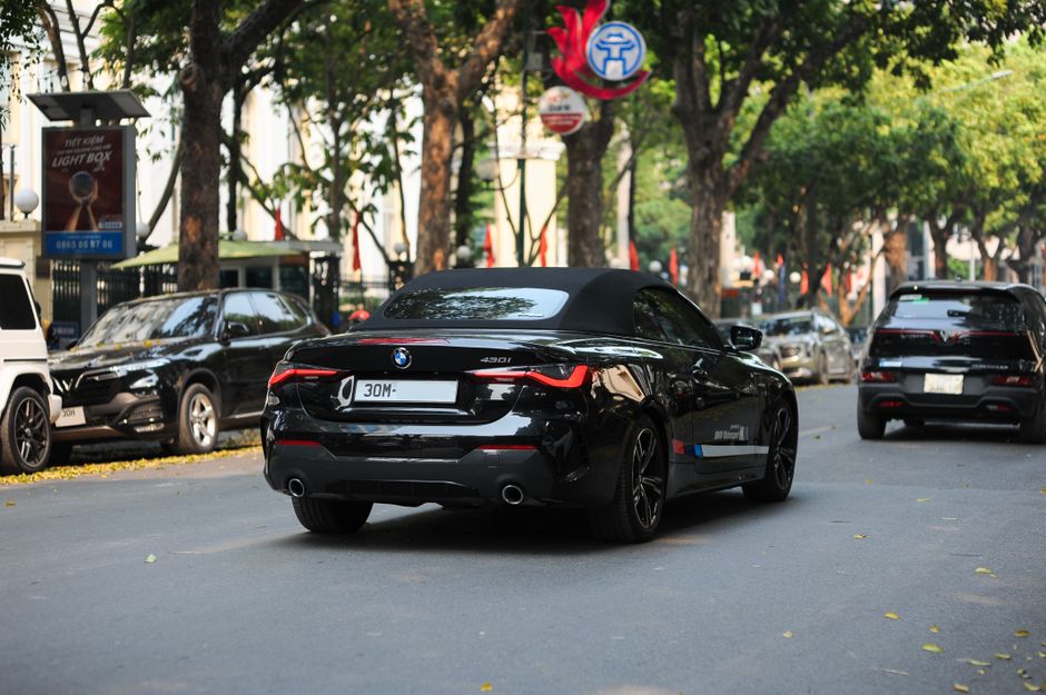 Black BMW 430i Cabriolet driving down a tree-lined urban street, daytime.