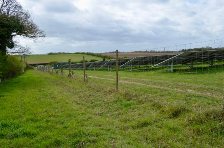 Solar panels installed in a rural field landscape under a cloudy sky.