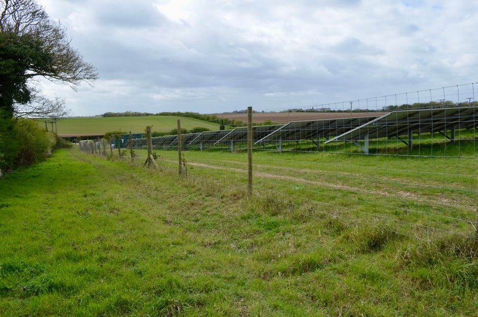 Solar panels installed in a rural field landscape under a cloudy sky.
