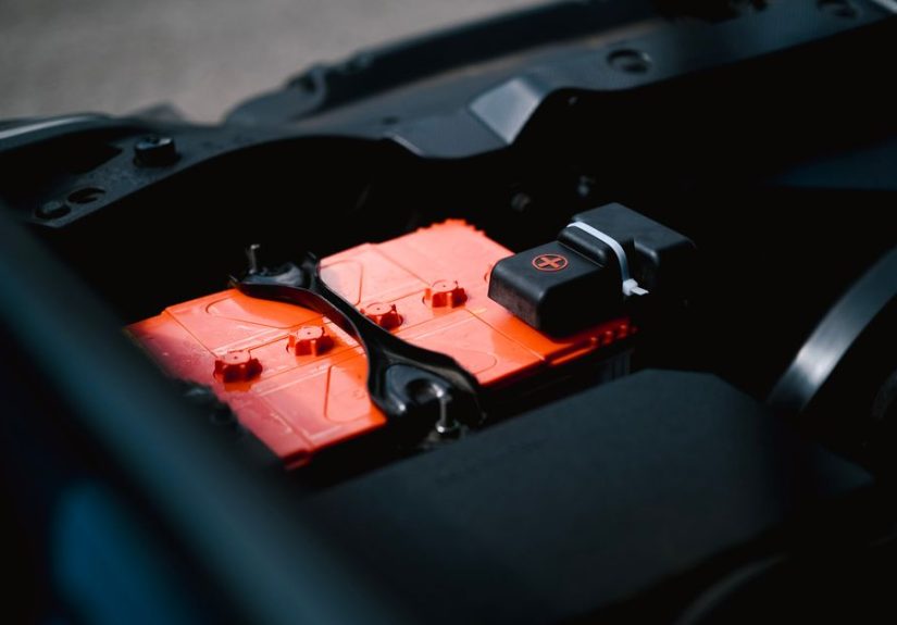 Detailed view of an orange car battery inside a vehicle's engine bay, highlighting its features.
