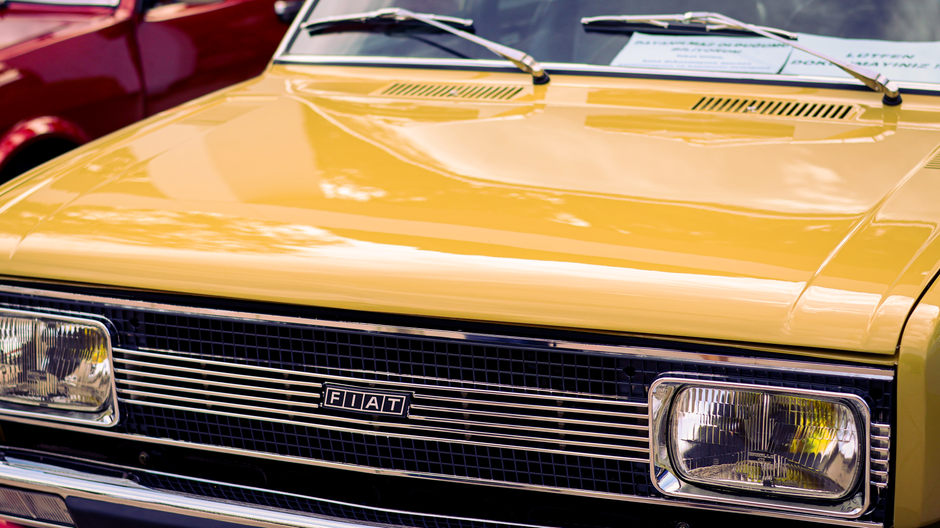 Closeup of a vintage yellow Fiat car's front grill and headlights.
