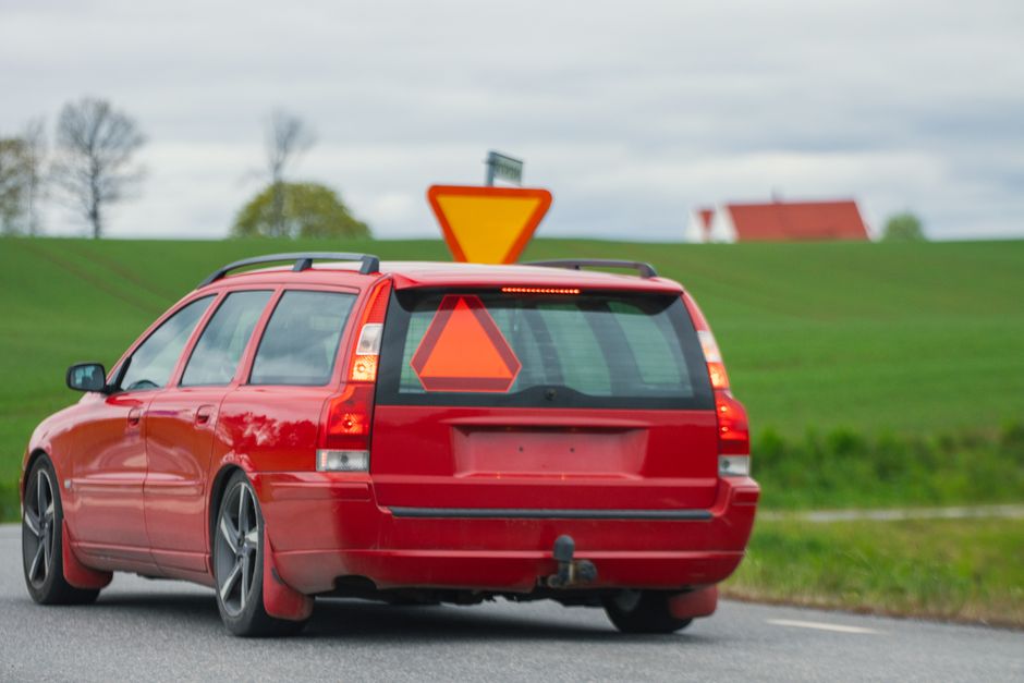 A red car drives on a countryside road in Jönköping, Sweden with a rural landscape.