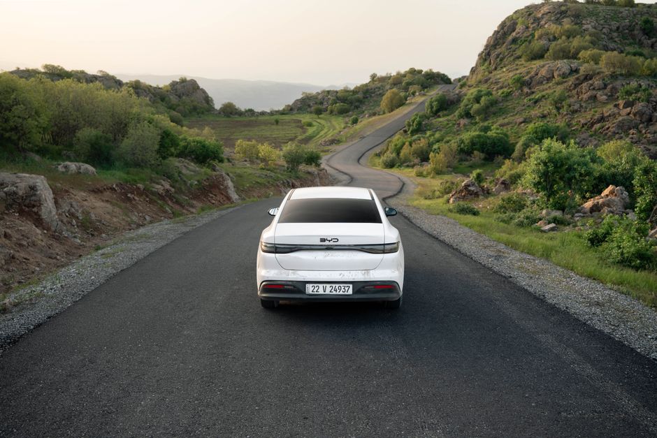 A white car travels down a winding road in the lush hills of Shaqlawa, Iraq, showcasing serene scenery.