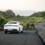 A white car drives on a winding road through scenic hills in Shaqlawa, Iraq during daylight.