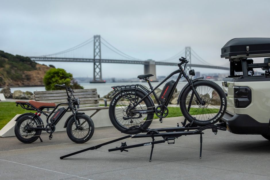 Electric bicycles parked near the iconic San Francisco Bay Bridge on a cloudy day.