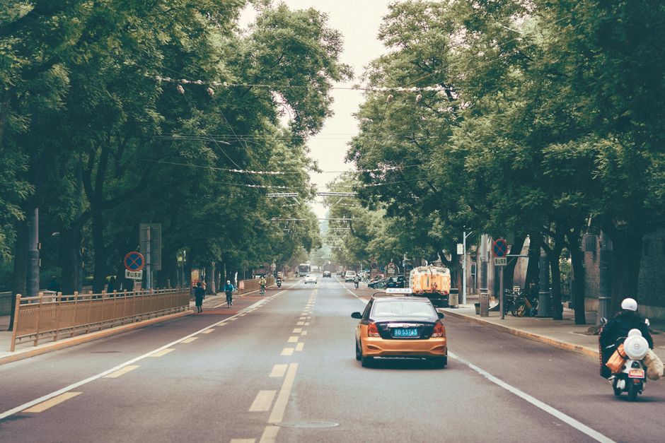 Scenic tree-lined street in Beijing, China, with cars and scooters under a tranquil sky.