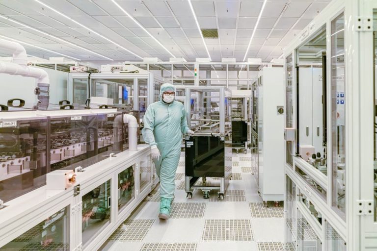Scientist in protective gear walking in a high-tech cleanroom laboratory environment.
