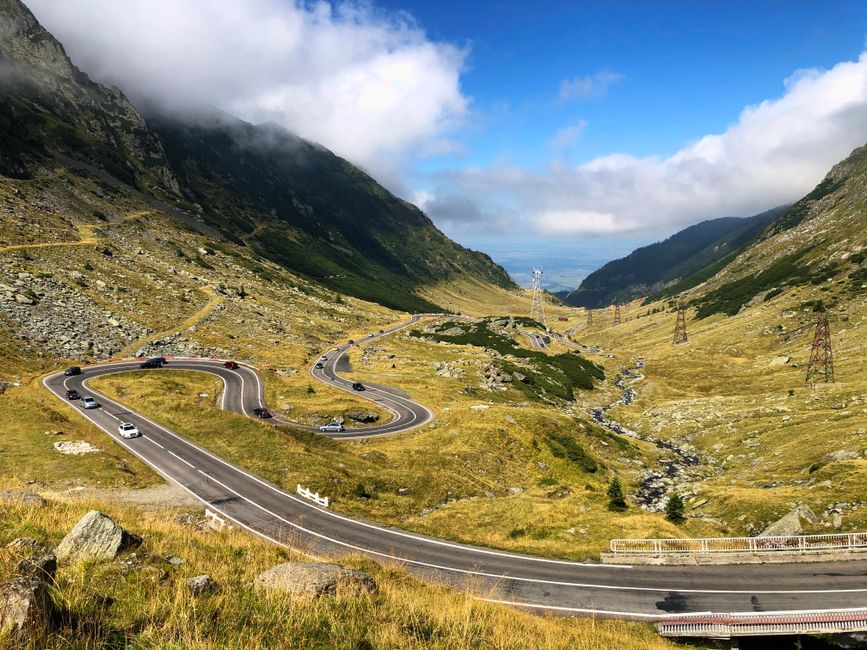 Scenic view of a winding road through mountains in Curtea de Argeș, Romania, under a clear summer sky.