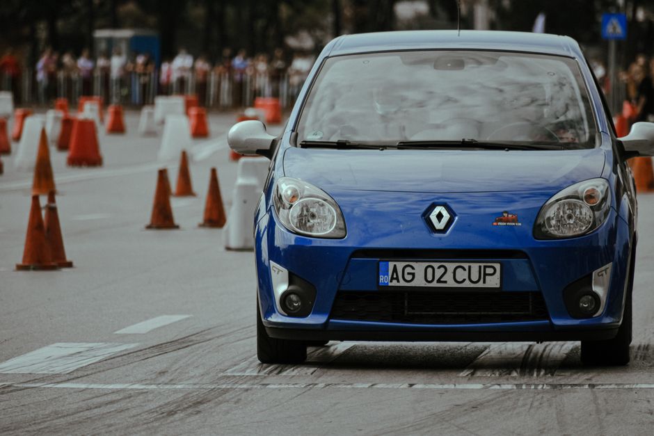 Modern blue automobile with headlights riding on pavement with marking lines near traffic cones on autodrome in city street with blurred background