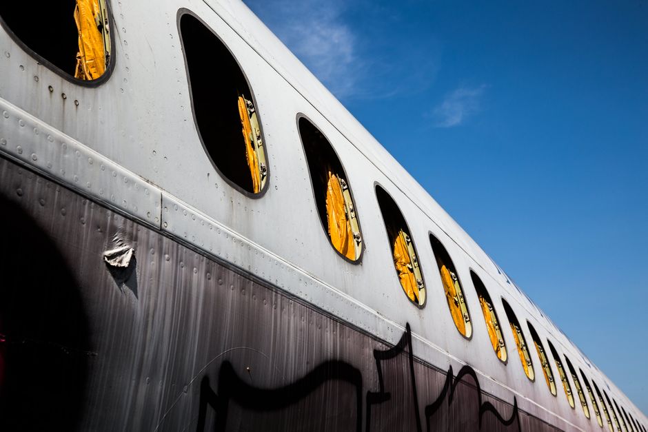 Close-up of a graffiti-marked abandoned airplane with open windows against a clear sky.