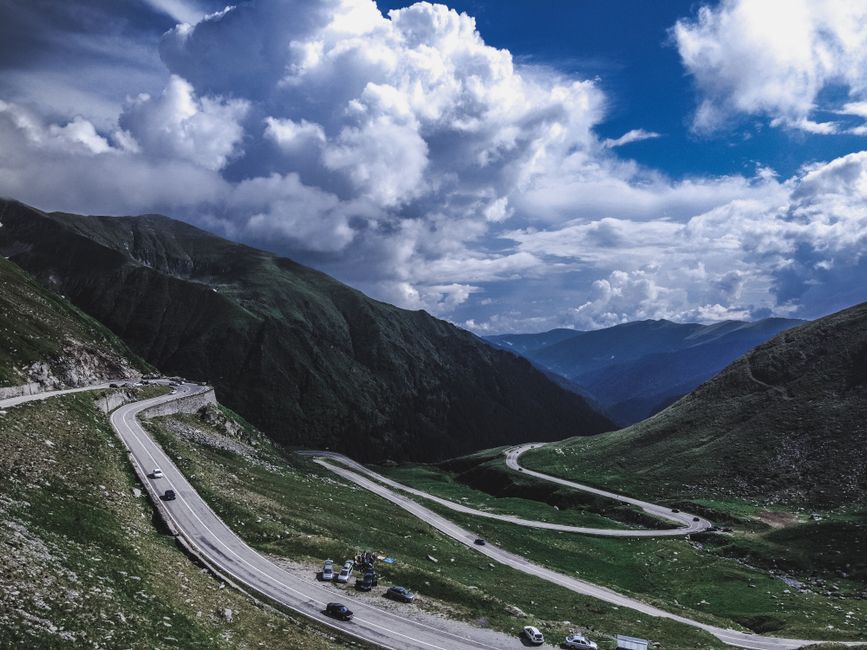 A mesmerizing aerial view of winding roads in Romania's Carpathian Mountains under dramatic clouds.