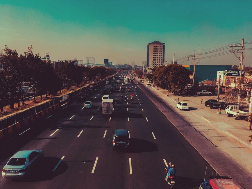 A bustling highway in Quezon City with vehicles and urban buildings under a clear sky.