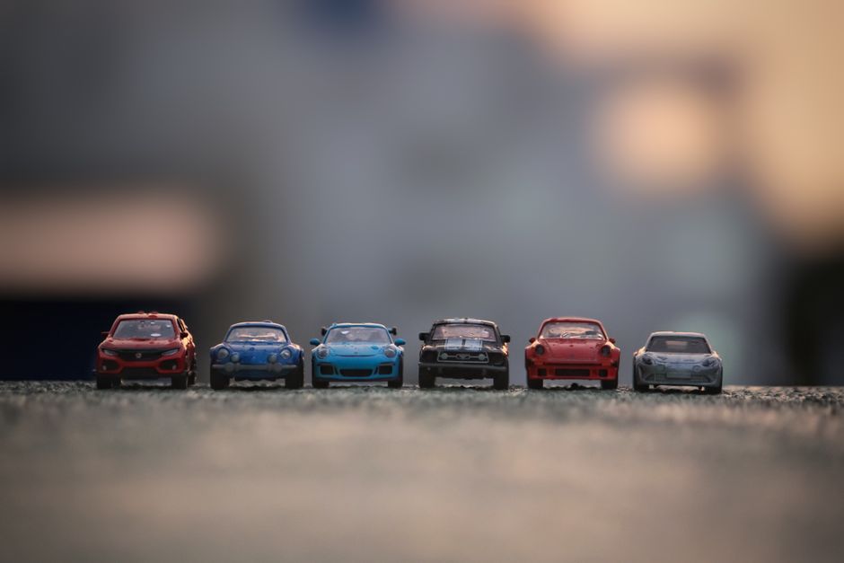 Close-up of six toy race cars lined up on asphalt with a blurred background.