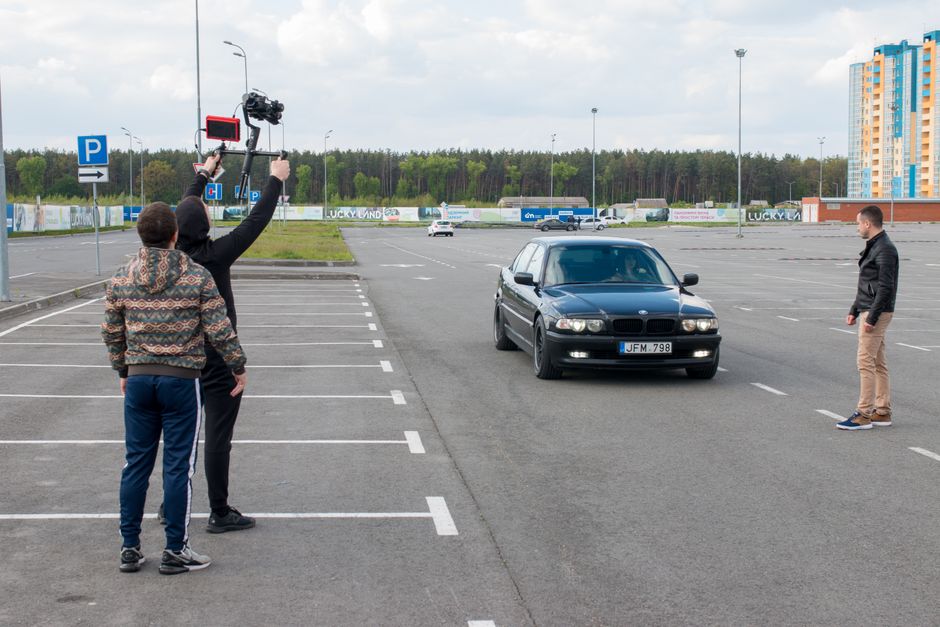 A film crew with a camera rig directs a car scene in an outdoor parking lot.