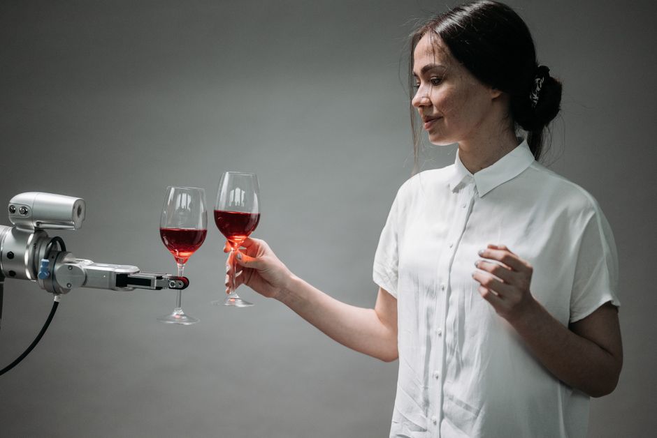 A woman and a robotic arm clink glasses of red wine, symbolizing technological harmony.