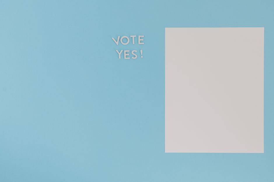 A minimalist concept image featuring 'Vote Yes' text and blank paper on a blue background.