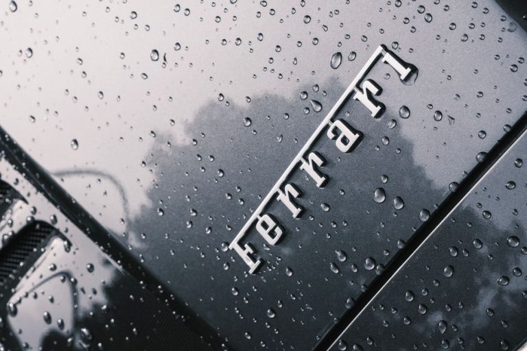 Close-up of a luxury Ferrari hood covered with raindrops, showcasing its sleek design.