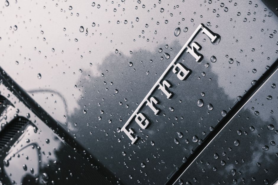 Close-up of a luxury Ferrari hood covered with raindrops, showcasing its sleek design.