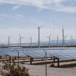 A renewable energy farm with wind turbines and solar panels under a clear sky.