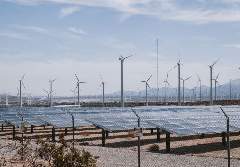 A renewable energy farm with wind turbines and solar panels under a clear sky.