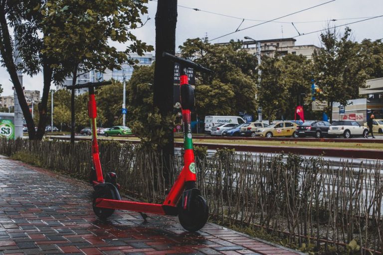 A vibrant red electric scooter parked on a wet sidewalk in Bucharest, showcasing urban mobility.