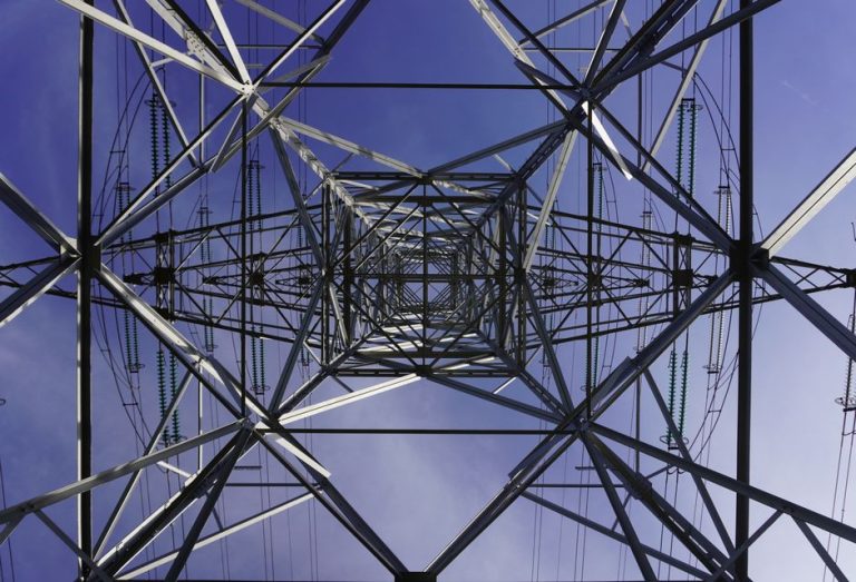 Low angle view of a transmission tower with geometric patterns against a clear blue sky.