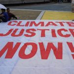 Large protest banner reading 'Climate Justice Now!' displayed outdoors during a demonstration.