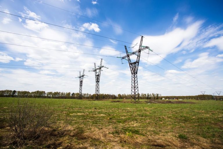 Scenic view of power lines crossing a green field under a bright blue sky.