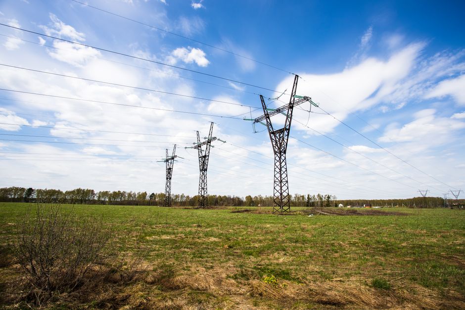 Scenic view of power lines crossing a green field under a bright blue sky.