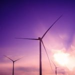 Three wind turbines silhouetted against a purple sunset sky, embodying renewable energy.