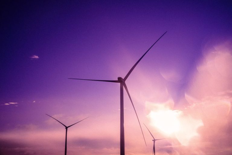 Three wind turbines silhouetted against a purple sunset sky, embodying renewable energy.
