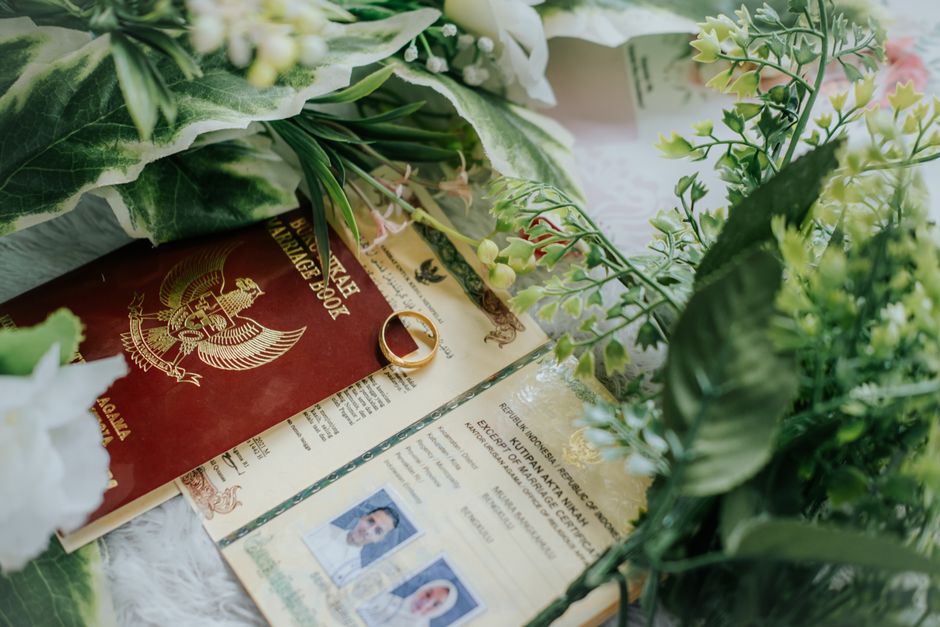 Close-up of marriage book and certificate adorned with greenery and wedding ring.