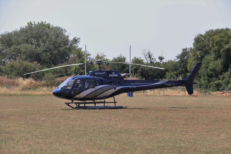 A helicopter parked in a grassy field on a clear day, surrounded by trees.