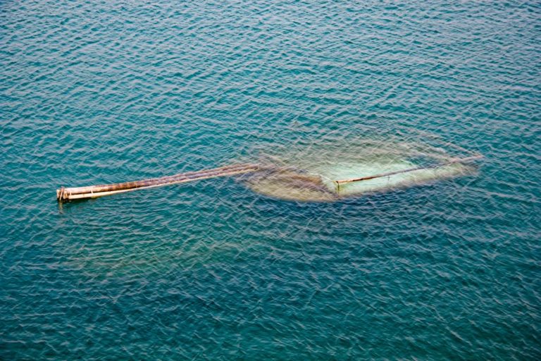 Aerial shot showing a submerged industrial platform with pipes extending into clear blue open water.