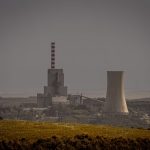 Distant view of a power plant with cooling towers amidst a vast landscape, illustrating energy production.