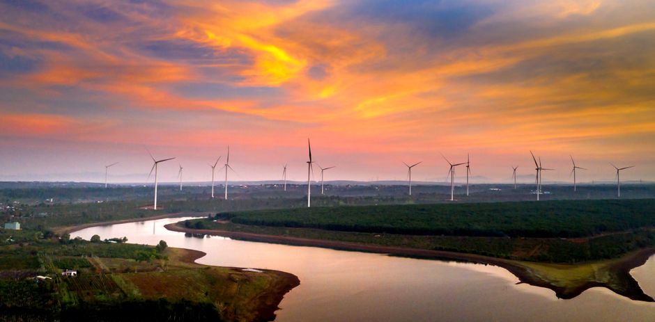 Aerial view of wind turbines in a vibrant sunset sky over a river and fields.