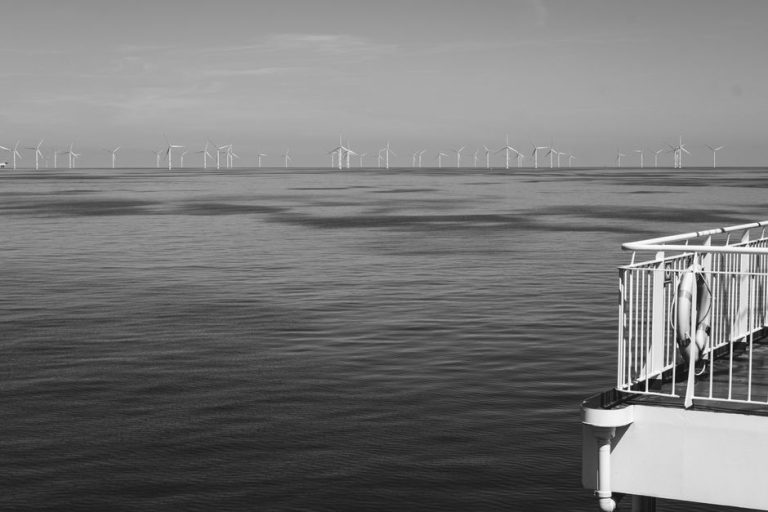 Black and white image of wind turbines in the ocean, symbolizing renewable energy.