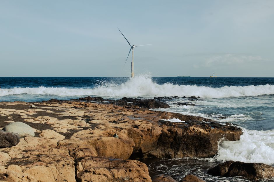 Wind turbine on a rocky ocean shore with waves crashing, showcasing renewable energy in nature.