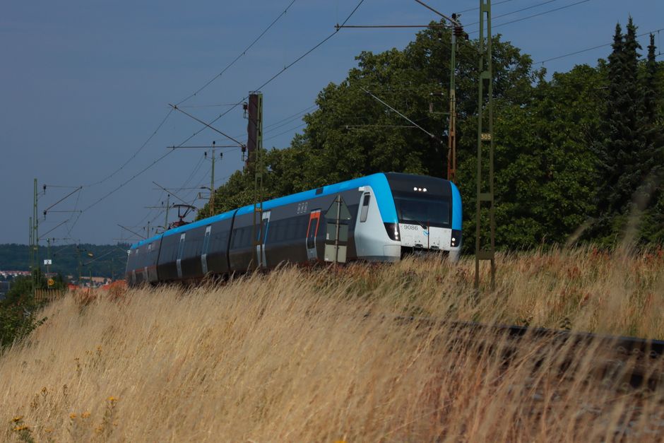 A sleek train traveling at speed through a scenic landscape with grassy fields and overhead power lines.