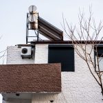 A minimalist building facade with air conditioner and bare winter trees, viewed from a low angle.