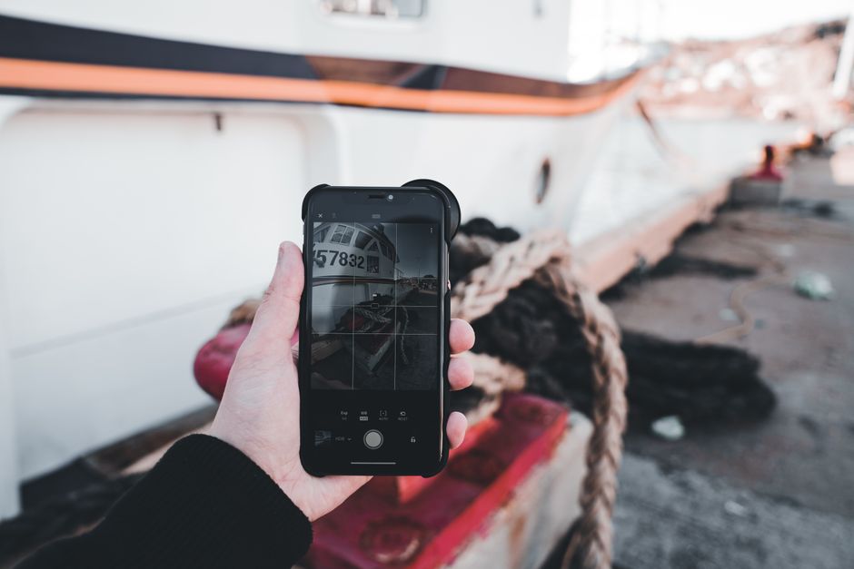 A person photographing a moored ship with a smartphone, emphasizing technology and travel.