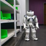 A humanoid robot standing in a modern corridor with shelves, representing futuristic technology.